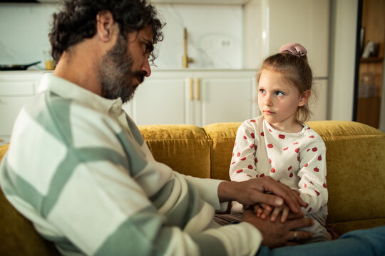 Father comforting worried daughter on home sofa