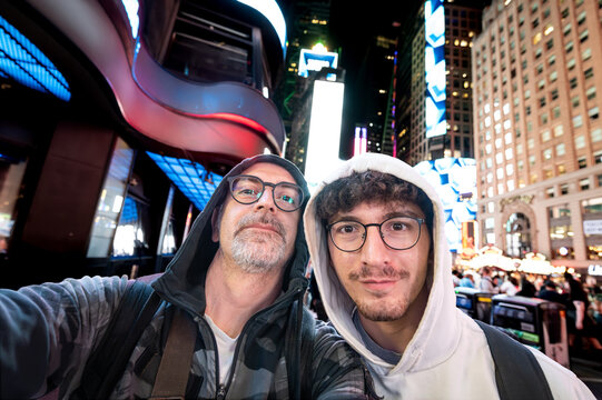 New york, usa august 21,2024. Two men smiling for a selfie in times square at night, surrounded by bright led screens, crowds and vibrant city lights