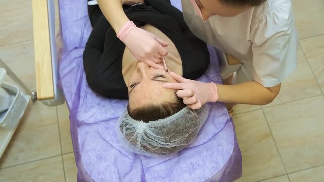 Top view dermatology session with ongoing facial injections in beauty clinic. Neuromodulator injections addressing forehead wrinkles and expression lines using controlled precision. Advanced anti