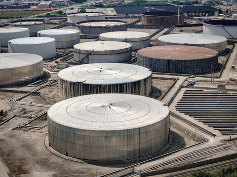 Aerial view of large industrial oil refinery and storage facility featuring massive cylindrical tanks and solar panel arrays at Polo Industriale San Martino, Piemonte, Italy.