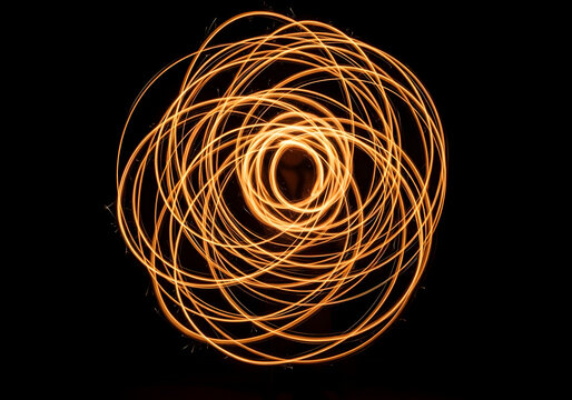 Abstract swirling light trails in golden orange hues, isolated on transparent background, created with slow shutter speed photography and motion blur.