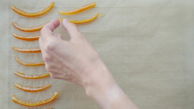 Hand arranges candied orange peel strips on parchment paper. Concept of homemade sweets and citrus dessert
