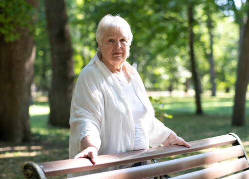 Old lady pensioner in city park on green nature background. Portrait of happy smiling senior woman