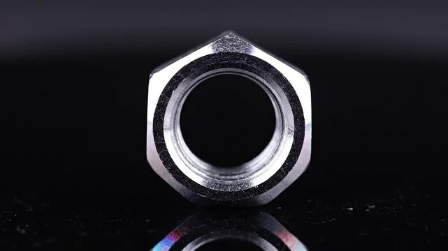 Shiny stainless steel hexagonal nut on a polished black surface with reflection