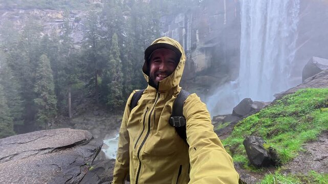 Young smiling hiker filming himself with an action camera while exploring the majestic and misty vernal fall along the mist trail during a memorable adventure in yosemite national park