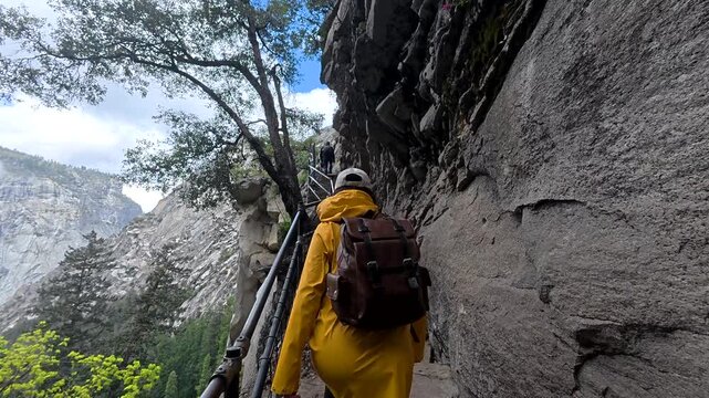 Young female hiker with a backpack walking up the challenging and narrow stone steps of the mist trail, heading towards vernal fall and nevada fall in yosemite national park, california