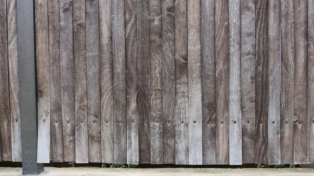 An old wooden fence made of vertical boards. The boards have a distinct natural grain pattern with wood grain, knots, and scuffs, as well as uneven gray, brown, and dark brown tones