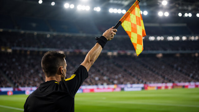 A vigilant assistant referee raises his flag during a competitive football match, a crucial signal that often precedes a whistle call in high-stakes games