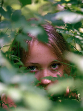 Young girl peeking through green foliage in natural light