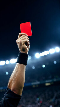 Referee holds up red card during soccer match at stadium during World Cup tournament, football game action with whistle