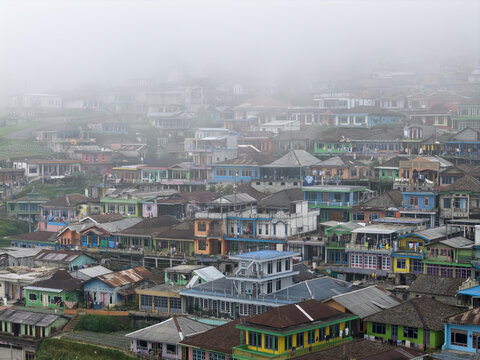 Aerial view of Nepal Van Java featuring colorful houses on a steep hillside shrouded in thick morning mist in Kecamatan Kaliangkrik, Jawa Tengah, Indonesia.