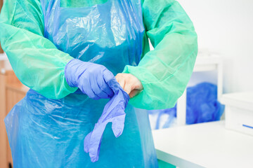 Fototapeta premium A medical professional wearing a protective gown puts on blue nitrile gloves in a clinical setting to ensure hygiene, sterility, and safety protocols during daily healthcare work