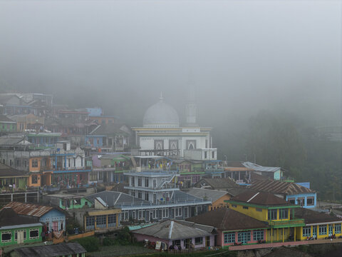 Aerial view of Nepal Van Java village featuring colorful houses and a prominent mosque shrouded in thick morning mist in Kecamatan Kaliangkrik, Jawa Tengah, Indonesia.