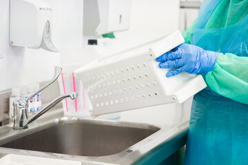 Naklejka premium A gloved worker sanitizing a plastic basket at a sink in a medical facility to emphasize the strict hygiene protocols and cleaning procedures required for a sterile environment