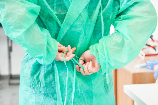 A dedicated medical professional ties their green protective gown strings behind their back at a hospital clinic to illustrate clinical preparation and strict safety protocols