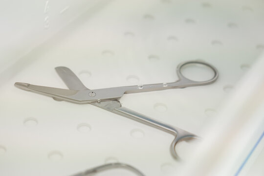 Medical bandage scissors soaking in a perforated plastic cleaning tray, demonstrating the sterile sterilization process for surgical tools in a clean and clinical healthcare setting