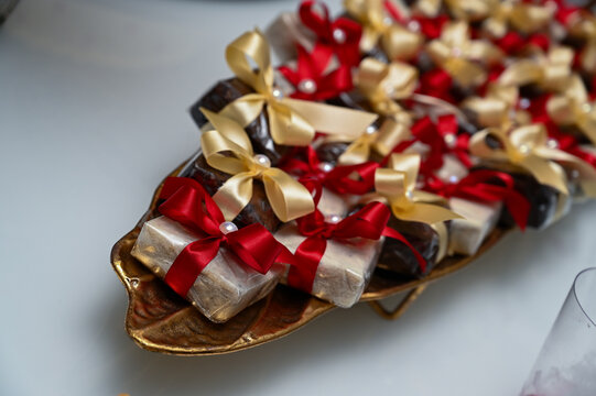 traditional brazilian bem casado wedding sweets on golden platter, wrapped party favors with red and gold ribbons, high angle view of artisanal confectionery desserts with copy space