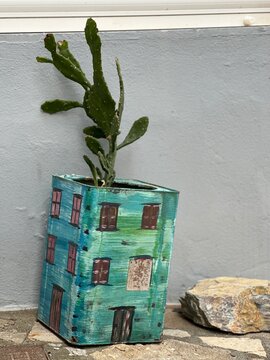 Plant grows in creative handmade pot shaped like a house in an outdoor space with a stone nearby