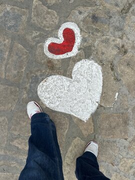 Hearts painted on stone pavement near feet in a public space during daytime
