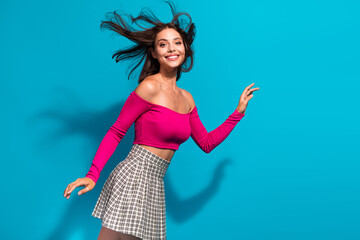 Young woman in a bright pink off the shoulder top and checkered skirt smiles against a vibrant blue...