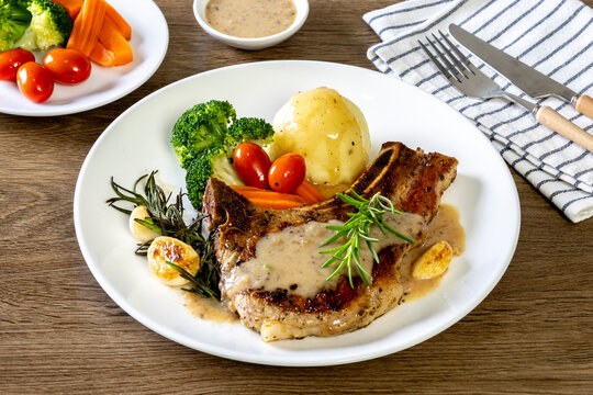  Grilled pork chop steak with baked potatoes, tomatoes and Broccoli, carrot on white plate