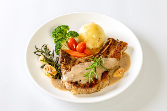  Grilled pork chop steak with baked potatoes, tomatoes and Broccoli, carrot on white plate