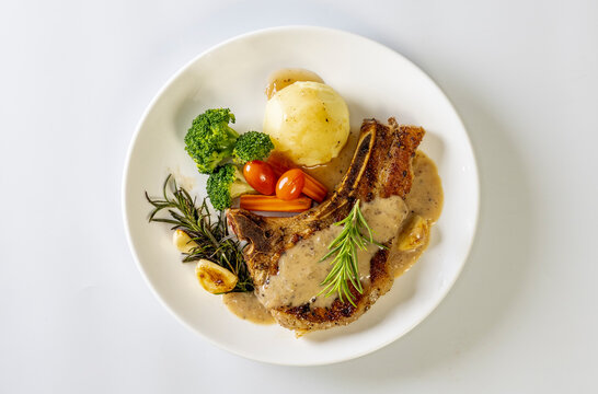  Grilled pork chop steak with baked potatoes, tomatoes and Broccoli, carrot on white plate