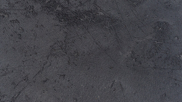 Rough full frame dark grey texture covered with multiple fine. Surface scratches and scuffs. Creating a weathered industrial or distressed metallic looking backdrop.