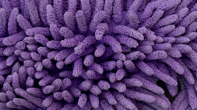Full-frame abstract macro texture of a bright purple microfiber mop cloth. The thick, soft shaggy fabric strands create a uniform pattern of vibrant organic shapes.