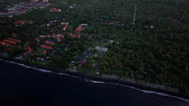 Drone tilting up from Tulamben coastline to reveal Mount Agung at dusk in Bali