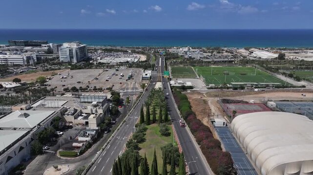 High angle aerial panoramic view of Matam high-tech park, soccer fields, and coastal infrastructure in Haifa, Israel, under a bright blue sky