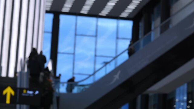 Modern airport interior with blurred travelers on escalators. People move quietly, focused on their journey. Blurred background highlights architectural design. Ideal for travel, transit
