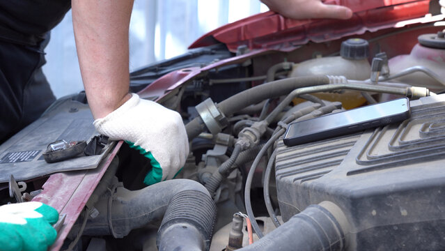 A Mechanic Working on an Engine Compartment with Tools and a Smartphone Nearby, Focusing on Maintenance and Repair Processes