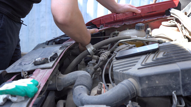 A Person Working on a Car Engine, Diagnosing Issues and Performing Maintenance with Tools in an Outdoor Setting