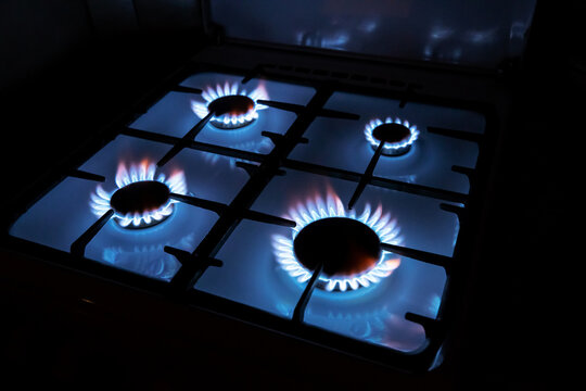 Four blue propane gas burners burning simultaneously on a kitchen stove range in the dark. kitchen cooking appliance
