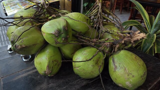 Large bunch of fresh young green coconuts resting on a dark wooden cart at an outdoor market, ready for sale. The tropical fruit is a popular source of refreshing and nutritious water