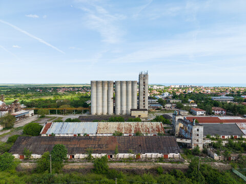 Aerial view of large concrete grain silos and weathered industrial warehouses under a clear blue sky in Balchik, Dobrich Province, Bulgaria.