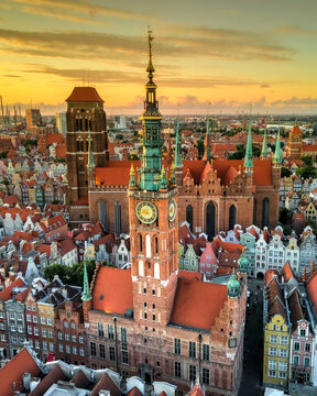Aerial view of the Main Town Hall and St. Mary's Church surrounded by historic red rooftops under a golden sunset sky in Gdansk, Pomeranian Voivodeship, Poland.