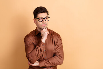 Obraz premium Thoughtful young man in glasses and brown shirt looking away, portrait of a professional thinking and contemplating ideas