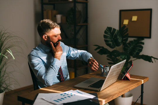 Businessman working in office feeling deadline pressure while checking time on his wristwatch