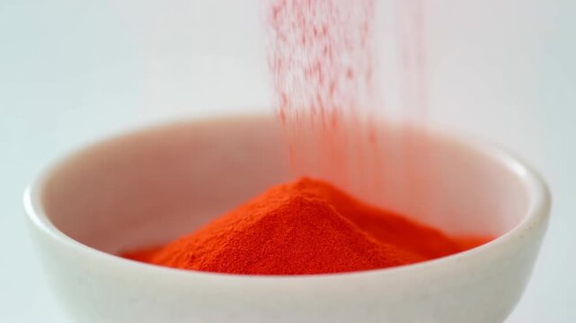 Slow motion shot of red paprika powder being poured into a white ceramic bowl
