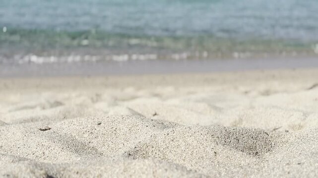 Cinematic rack focus from golden sand ripples to crystal-clear turquoise sea and blue horizon. Kal'e Moru beach, Quartu Sant'Elena, Sardinia, Italy. Cinematic mode, bright morning light, June.