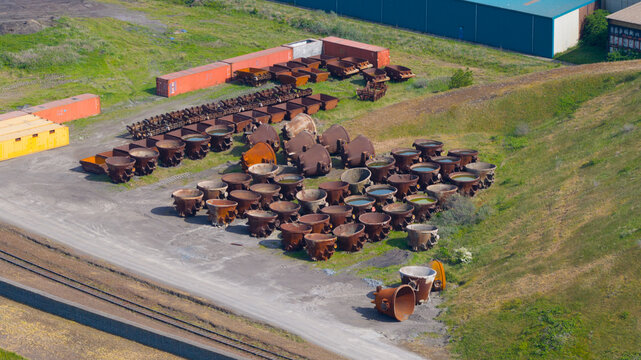 Aerial view of large rusty metal ladles and shipping containers at the Tata Steel industrial site near a grassy embankment in Velsen-Noord, Noord-Holland, Netherlands.