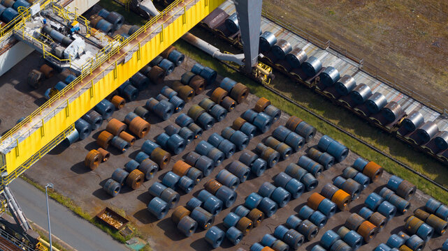 Aerial view of Tata Steel industrial site with rows of large steel coils stored outdoors near a yellow crane and railway tracks Velsen-Noord, Noord-Holland, Netherlands.