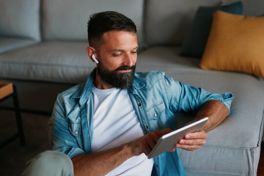 Casual adult browsing digital content on a tablet while sitting comfortably on the floor beside a sofa