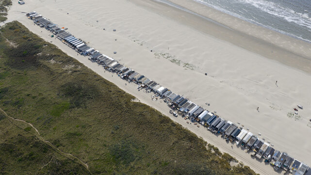 Aerial view of a long row of beach huts along the sandy coastline with grassy dunes and the North Sea waves in Velsen-Noord, North Holland, Netherlands.