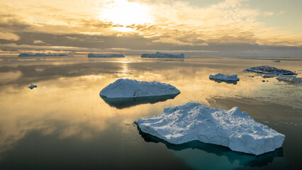 Floating icebergs on calm golden water at sunset near Ilulissat, Avannaata, Greenland, with dramatic clouds and arctic reflections © vadim.nefedov
