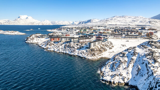 Winter aerial cityscape of Nuuk with colorful houses, apartment buildings, rocky islands, blue ocean and snow-covered arctic landscape