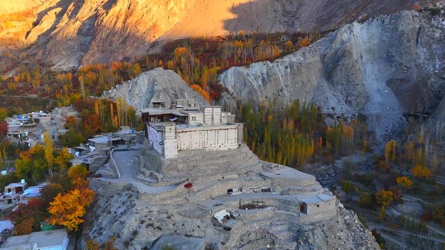 Aerial view of Baltit Fort surrounded by autumn trees and rugged mountains during golden hour in Karimabad, Gilgit Baltistan, Pakistan.