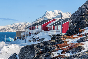 Colorful red residential houses on a snowy rocky hillside above the blue sea with arctic mountains and clear winter sky in Nuuk, Sermersooq, Greenland © vadim.nefedov